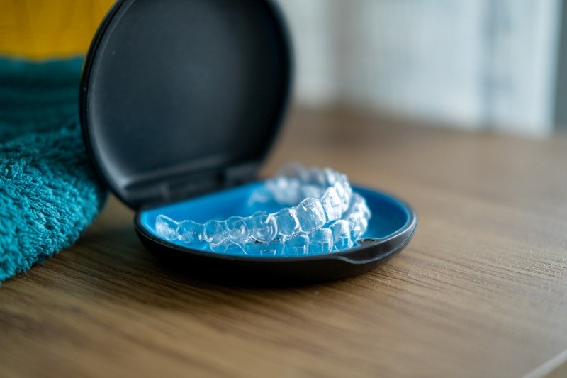 A set of Invisalign aligners rests in a sleek black and blue case on a wooden surface, with a teal towel partially visible in the background.